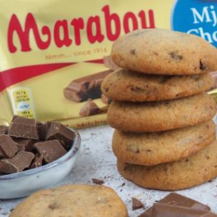 Gestapelte Cookies mit Marabou-Vollmilchschokolade Stückchen, daneben Schokostücke in einer Schale und eine Marabou King Size Vollmilch Tafel in goldener Verpackung