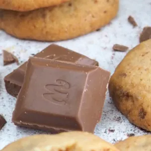 Einzelner Cookies mit Marabou-Vollmilchschokolade Stückchen, daneben und mittig im Fokus ganze Marabou Schokostücke