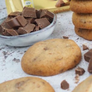 Gestapelte und einzelne Cookies mit Marabou-Vollmilchschokolade Stückchen, daneben Schokostücke in einer Schale und eine Marabou King Size Vollmilch Tafel in goldener Verpackung