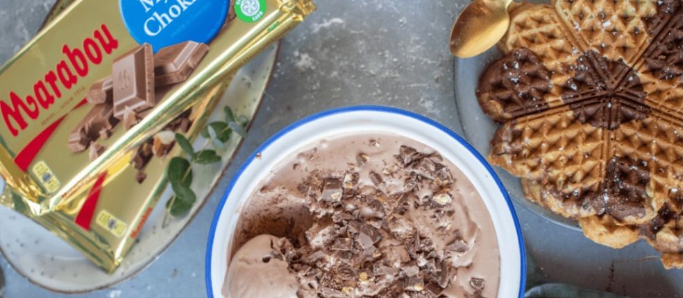 Ei Schokoladeneis mit Marabou-Stückchen in einer Schale, rechts daneben eine marmorierte Waffel und links zwei Marabou Vollmilch-Tafeln