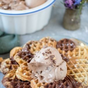 Ein Schokoladeneis mit Marabou-Stückchen in einer Schale, davor eine marmorierte Waffel und auf der Waffel eine Kugel des Eises