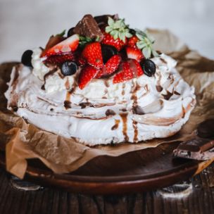 Pavlova mit Sahne, frischen Beeren, Marabou Stückchen und Schokoladensoße,