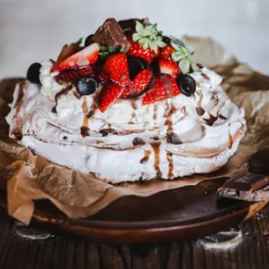Pavlova mit Sahne, frischen Beeren, Marabou Stückchen und Schokoladensoße,