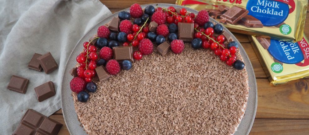 No-Bake-Schoko-Cheesecake mit Schokoraspeln, frischen Beeren und Marabou-Schokoladenstücken, serviert auf Teller mit Marabou King Size Tafeln im Hintergrund