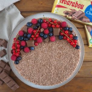 No-Bake-Schoko-Cheesecake mit Schokoraspeln, frischen Beeren und Marabou-Schokoladenstücken, serviert auf Teller mit Marabou King Size Tafeln im Hintergrund