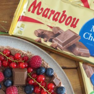 No-Bake-Schoko-Cheesecake mit Schokoraspeln, frischen Beeren und Marabou-Schokoladenstücken, serviert auf Teller mit Marabou King Size Tafeln im Hintergrund